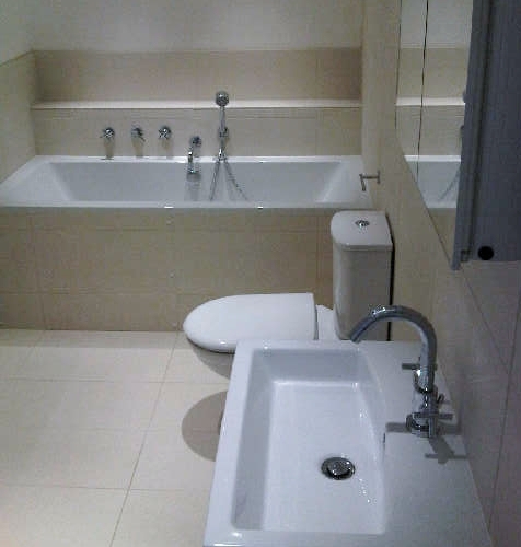 Bathroom with no windows and no natural light, using spot lights, mirrors and neutral coloured wall and floor tiles to create a feeling of light and space